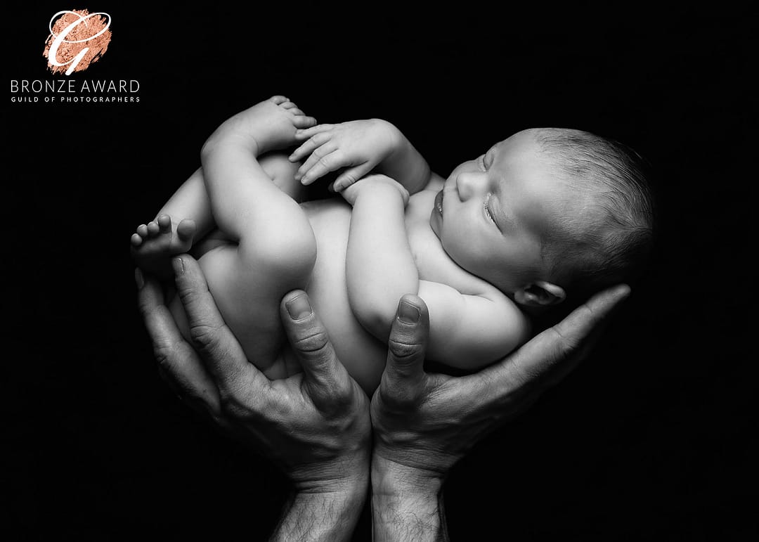 Award winning newborn photographer sutton coldfield, black and white image of newborn baby in dad's hands. Newborn photo taken by Sutton Coldfield newborn photographer Nicki Byrne Photography, newborn photographer birmingham