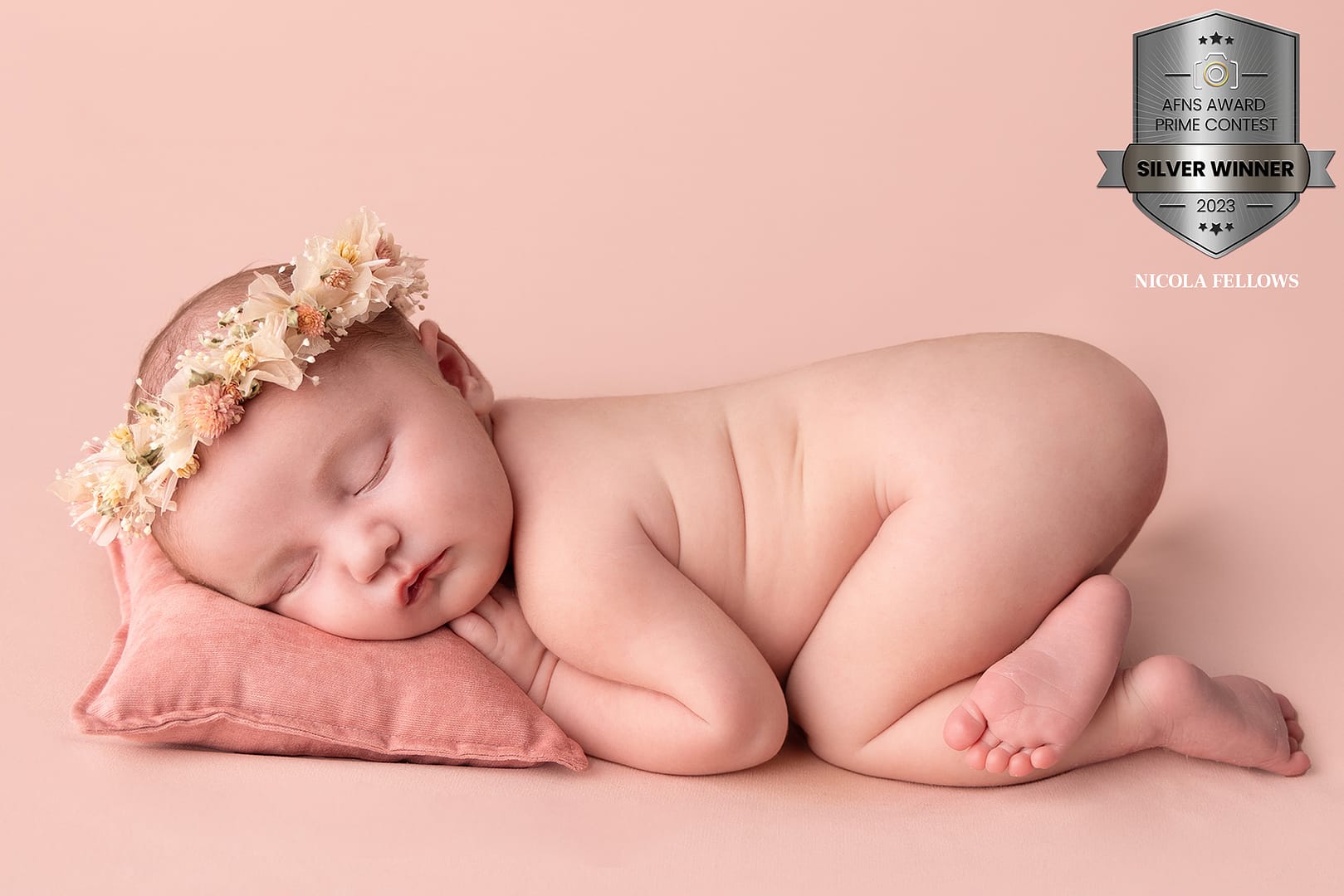 award winning image of baby girl lying on her tummy on a pale pink background with a pink pillow and floral halo. Taken by newborn photographer Sutton Coldfield baby photographer birmingham
