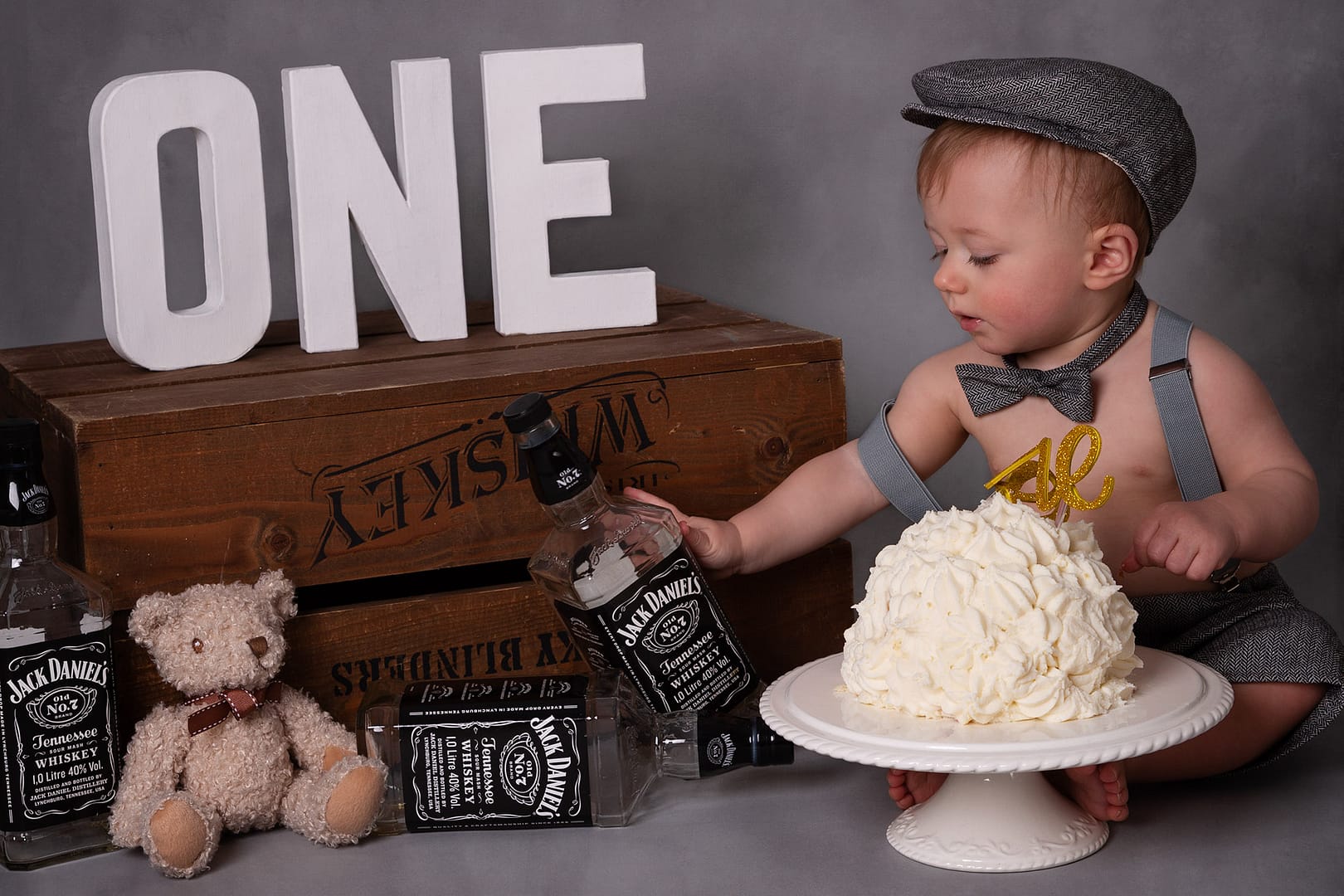 Peaky Blinders themed cake smash, boy sat reaching for empty bottles.  Cake smash photographer Sutton Coldfield birmingham
