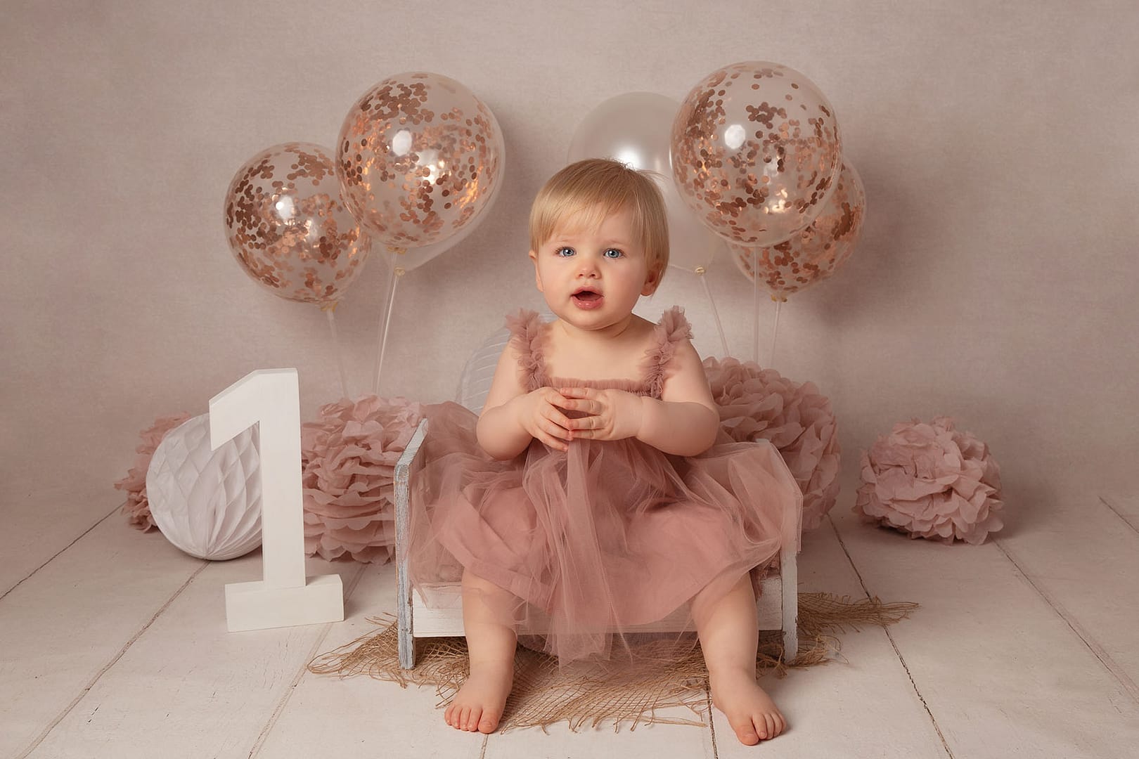 first birthday pictures with a rose gold and vintage theme, little girl sat on a bed smiling during her cake smash, photographer Sutton Coldfield birmigham