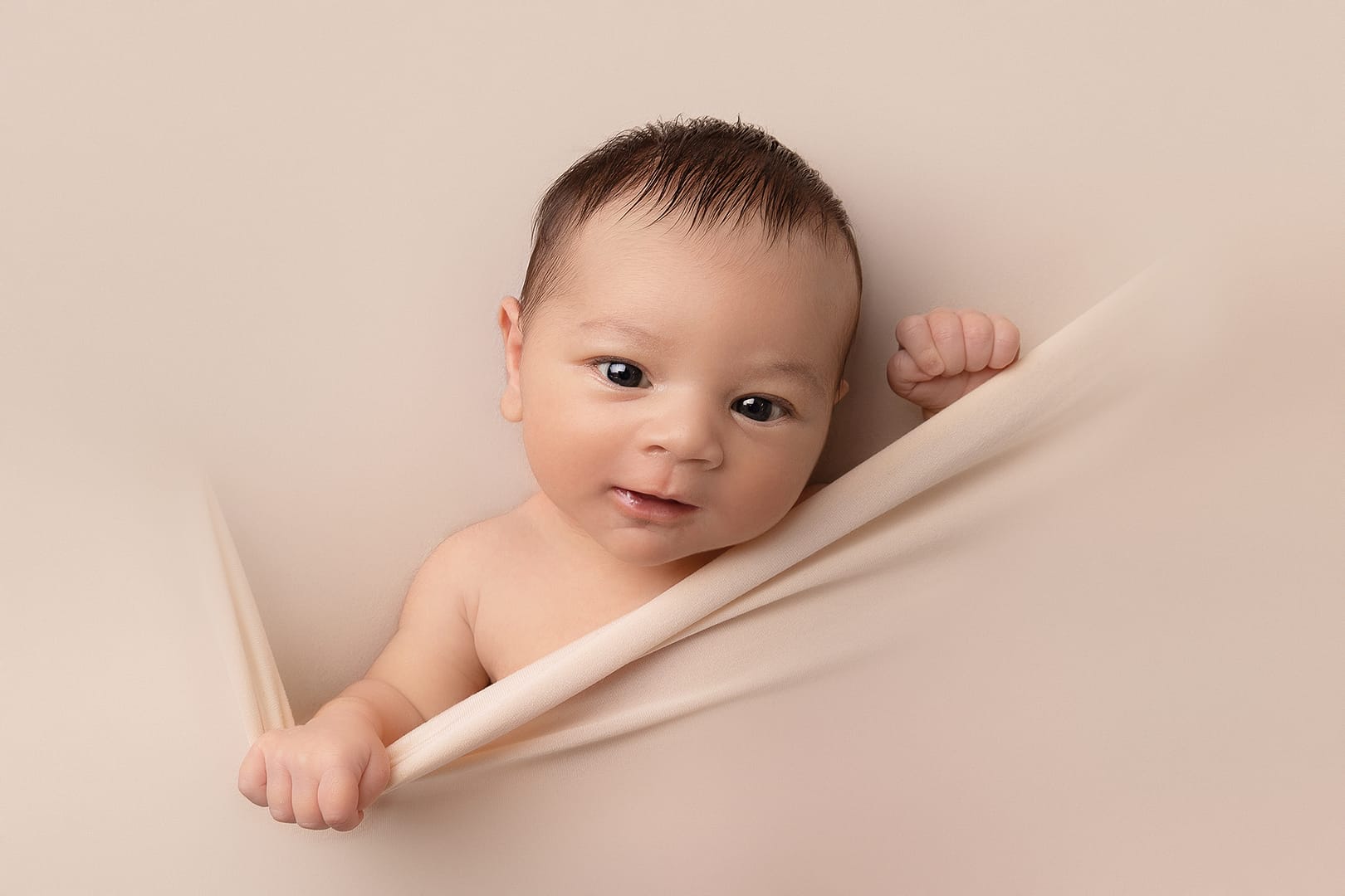 newborn baby looking at the camera smiling, peaking out from the backdrop.  Photograph taken by newborn photographer Nicki Byrne Photography, newborn photographer Sutton Coldfield birmingham