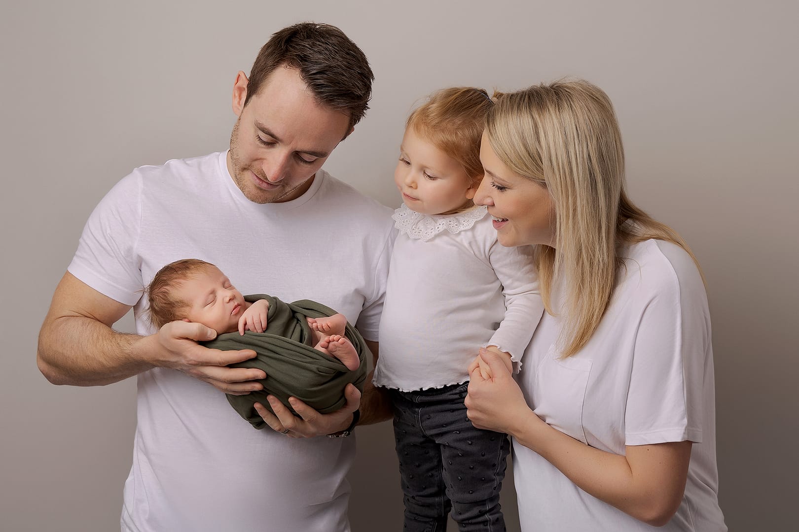 First family photo - Dad holding newborn baby boy while dad, mom and toddler sister are smiling at him.  Image taken by newborn photographer Nicki Byrne photography, newborn photographer Sutton Coldfield birmingham