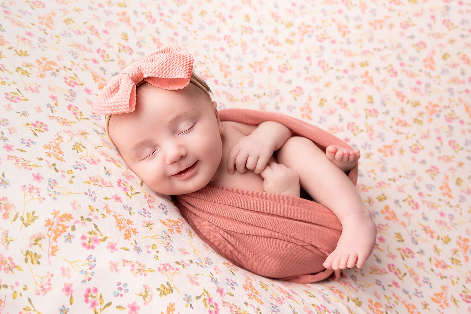 beautiful newborn baby girl swaddled with her legs out, sleeping peacefully on a floral backdrop.  Image taken by newborn photographer Nicki Byrne Photography, newborn photographer Sutton Coldfield birmingham
