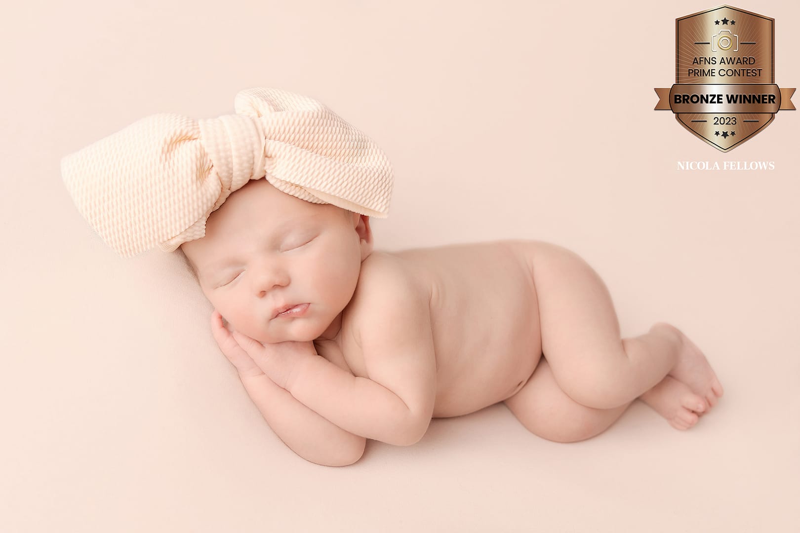 photograph of a beautiful baby girl lying on her side with a big cream bow on her head.  Photograph taken by newborn photgrapher Nicki Byrne Photography, newborn photographer Sutton Coldfield birmingham