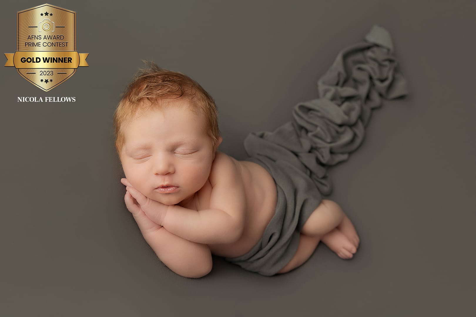 gorgeous baby boy lying on a khaki grey backdrop with a wrap around his tummy. He has his hands placed together under his cheek and is sleeping peacefully. Taken by Sutton Coldfield award winning newborn photographer, Nicki Byrne Photography - newborn photographer birmingham