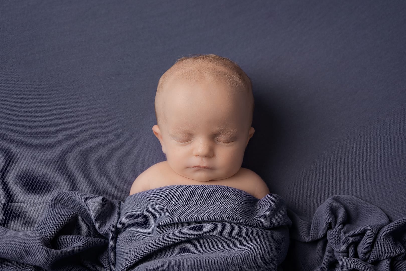 Newborn baby boy wrapped in blue material asleep.  Images taken by newborn photographer Nicki Byrne Photography, Sutton Coldfield, Birmingham
