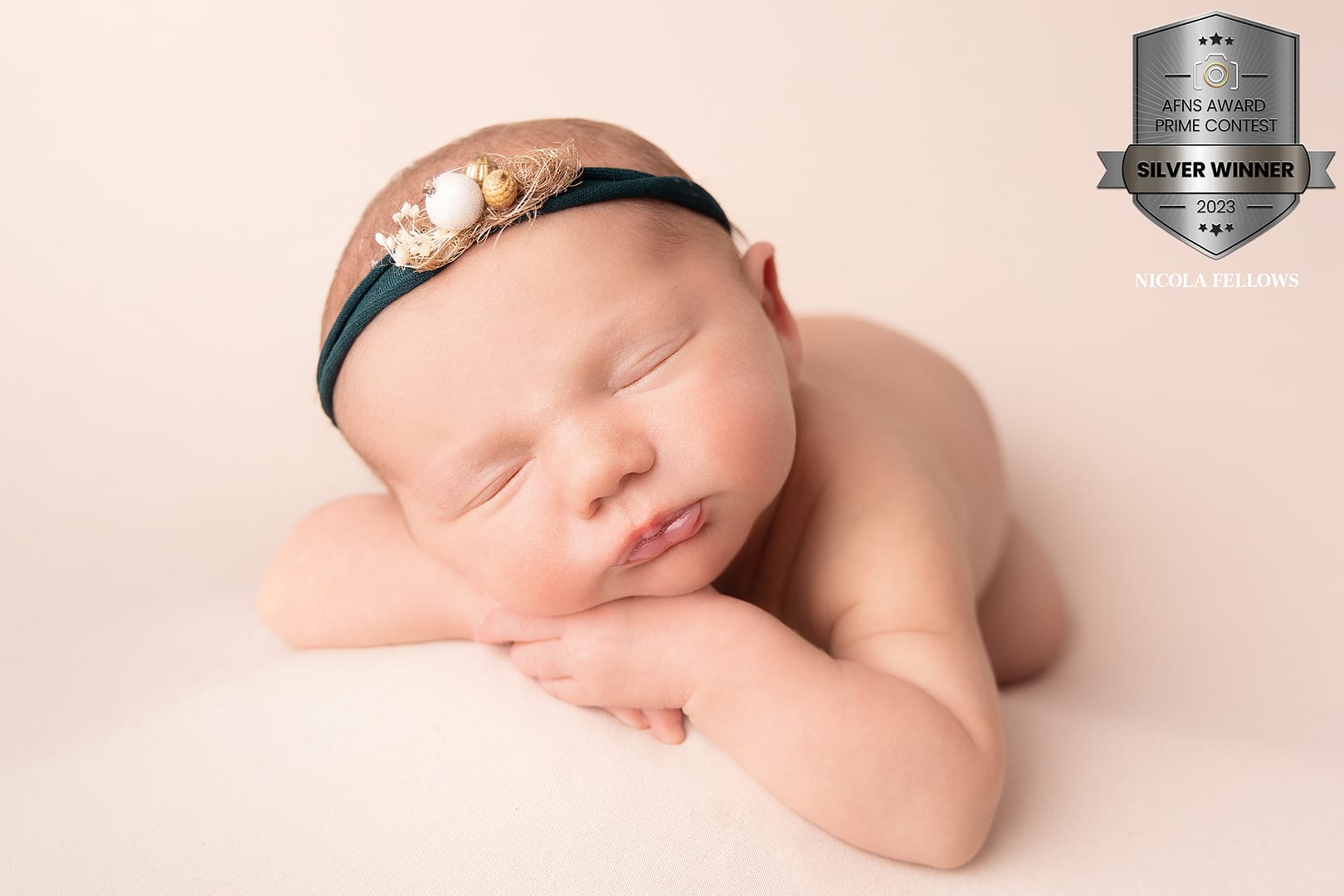 Award winning newborn photo. Baby lying head on hands on a cream backdrop with a forest green headband on.