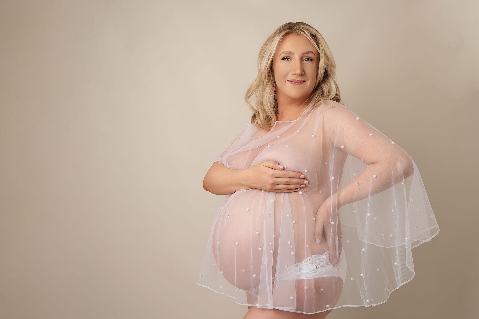 beautiful mother-to-be standing with a tulle cape over her, hand on one hip.  Taken by award winning photographer Nicki Byrne Photography, maternity photographer Sutton Coldfield birmingham