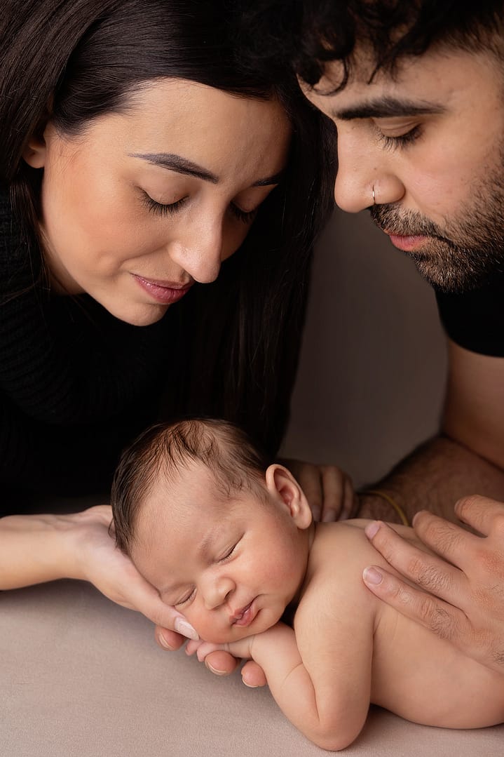 Family photographer - parents looking down at newborn baby fast asleep.  Photograph taken by newborn photographer Nicki Byrne Photography - newborn photographer birmingham