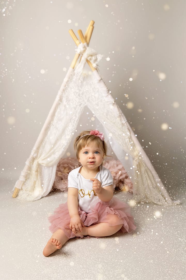 One year old celebrating her birthday infant of a white teepee at the start of her Cake Smash in Sutton Coldfield Birmingham